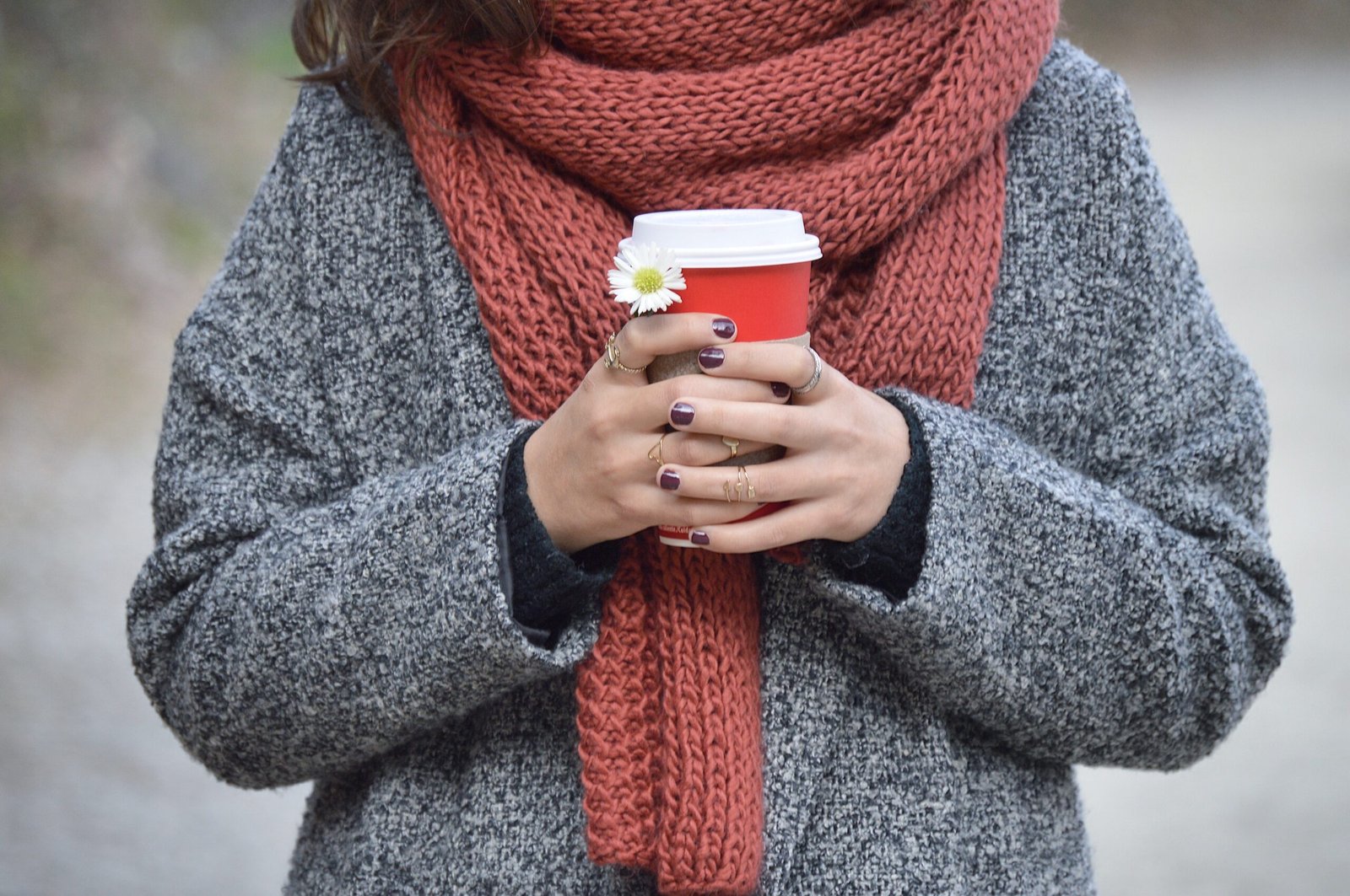 Person in a cozy scarf holding a to-go coffee cup with a small daisy tucked into it